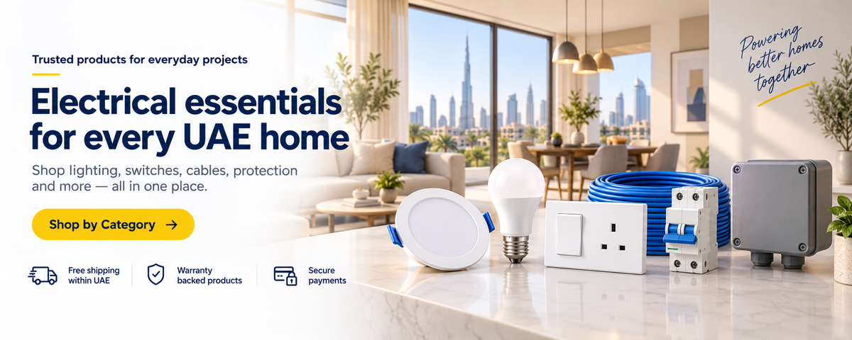 Promotional banner for electrical home essentials, showing a light bulb, switch, cable reel, fuse holder, and socket on a countertop in a modern living room setting with a city skyline background.