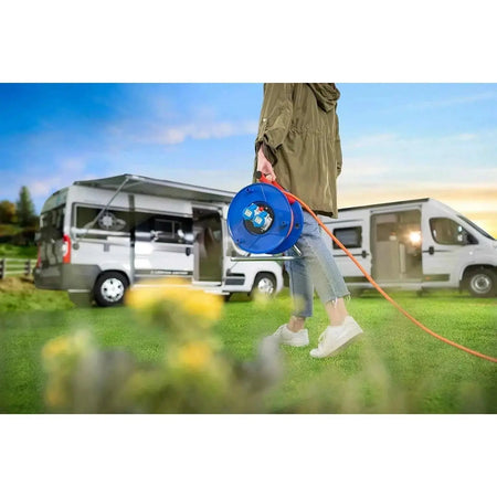 Brennenstuhl Garant 2-socket cable reel, blue IP44, 25m, carried by a person outdoors near camper vans. UAE