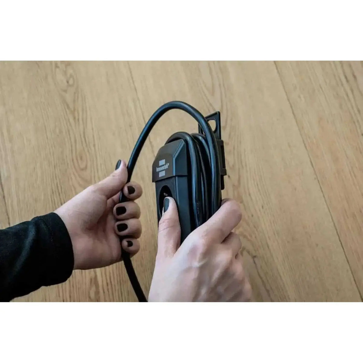 Brennenstuhl Premium Line Multistandard 5-way extension cord, 3m, black/grey, held by hands on a wooden floor UAE